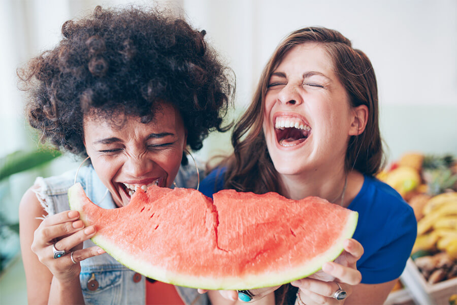 Frauen essen gemeinsam ein Stück Wassermelone und lachen