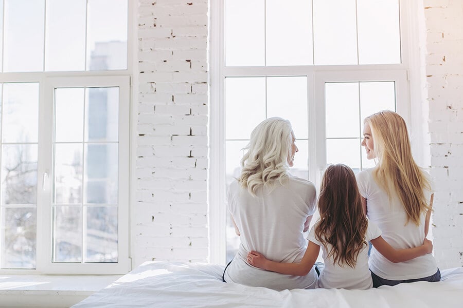Drei Generationen Frauen sitzen gemeinsam auf einem Bett